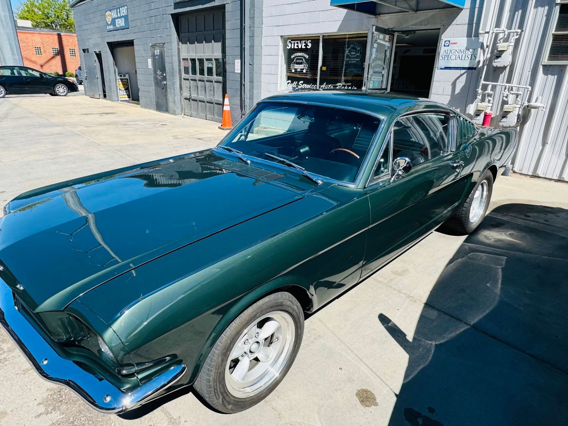 Green classic coupe parked outside a garage in bright sunlight