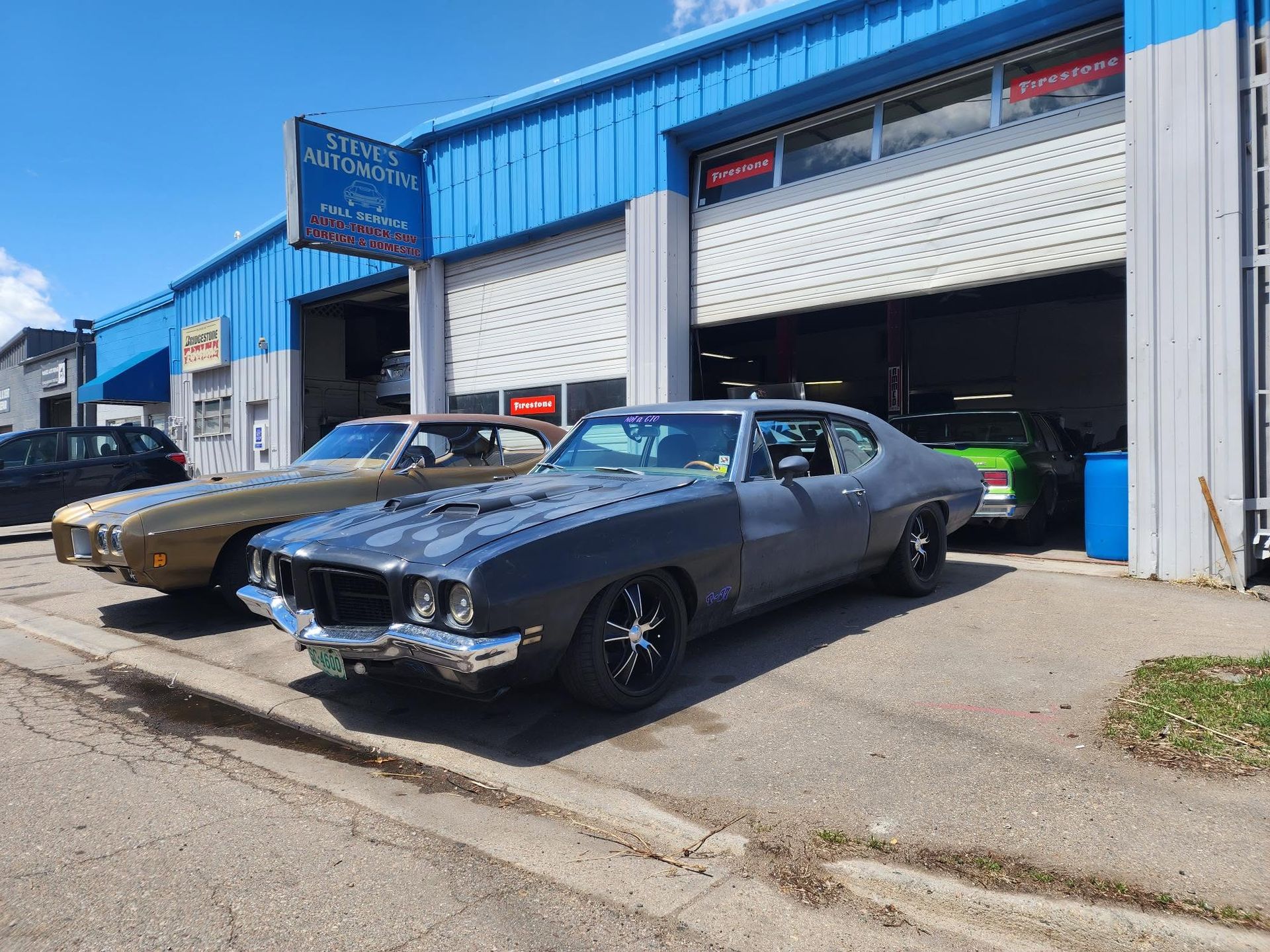 Classic cars parked outside a blue auto shop with garage doors open