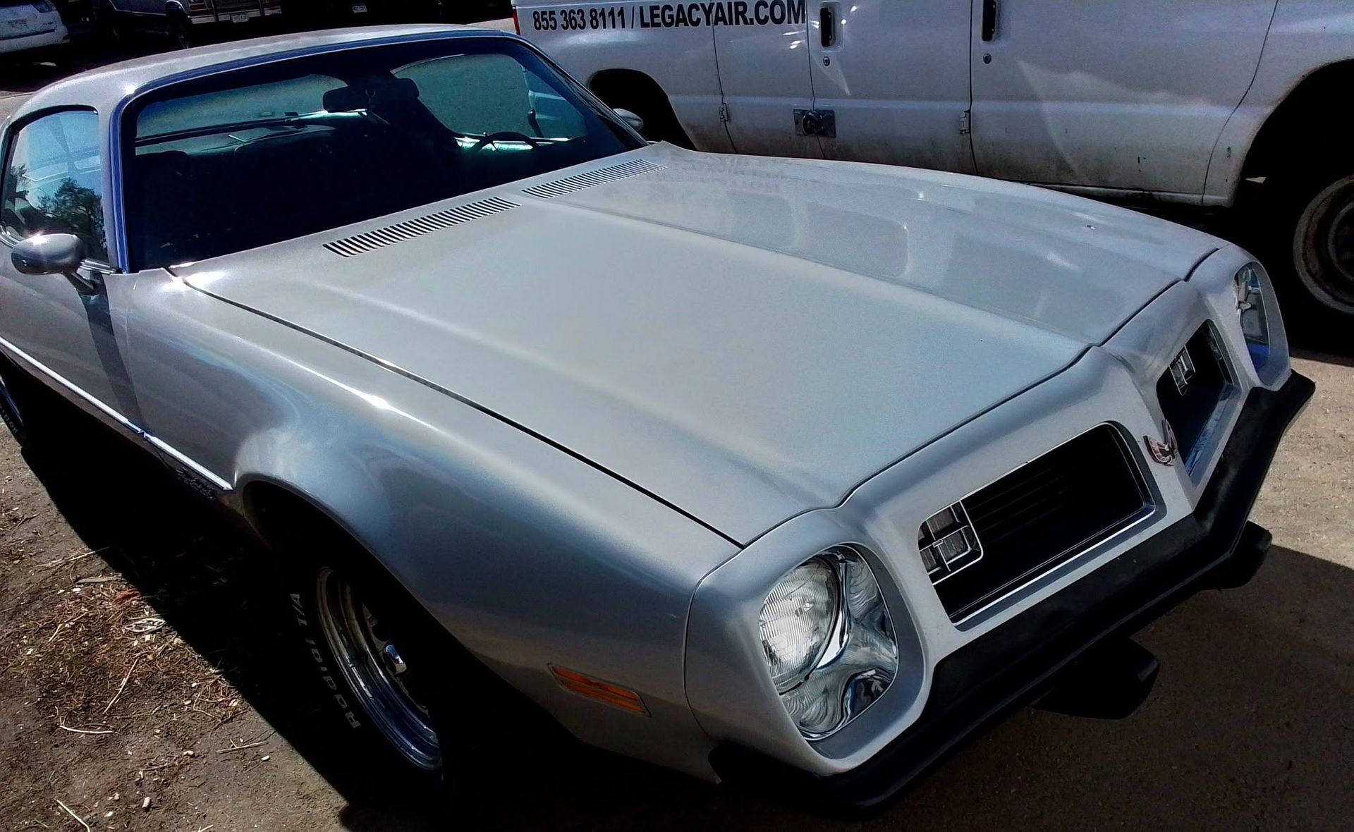 Classic silver car parked outdoors in bright sunlight, front-left view