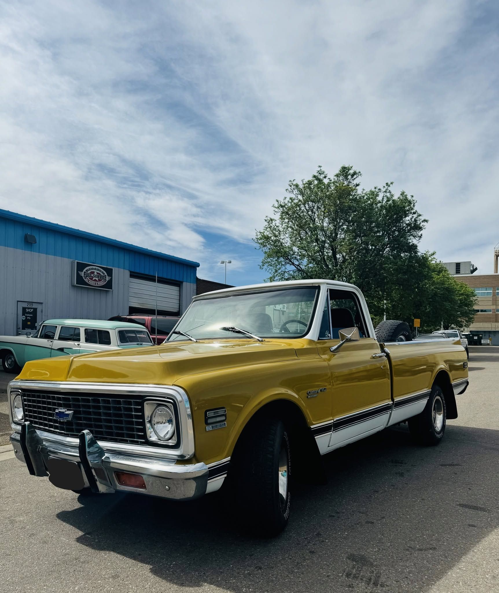 Yellow vintage pickup truck parked outdoors in front of a blue building under a partly cloudy sky