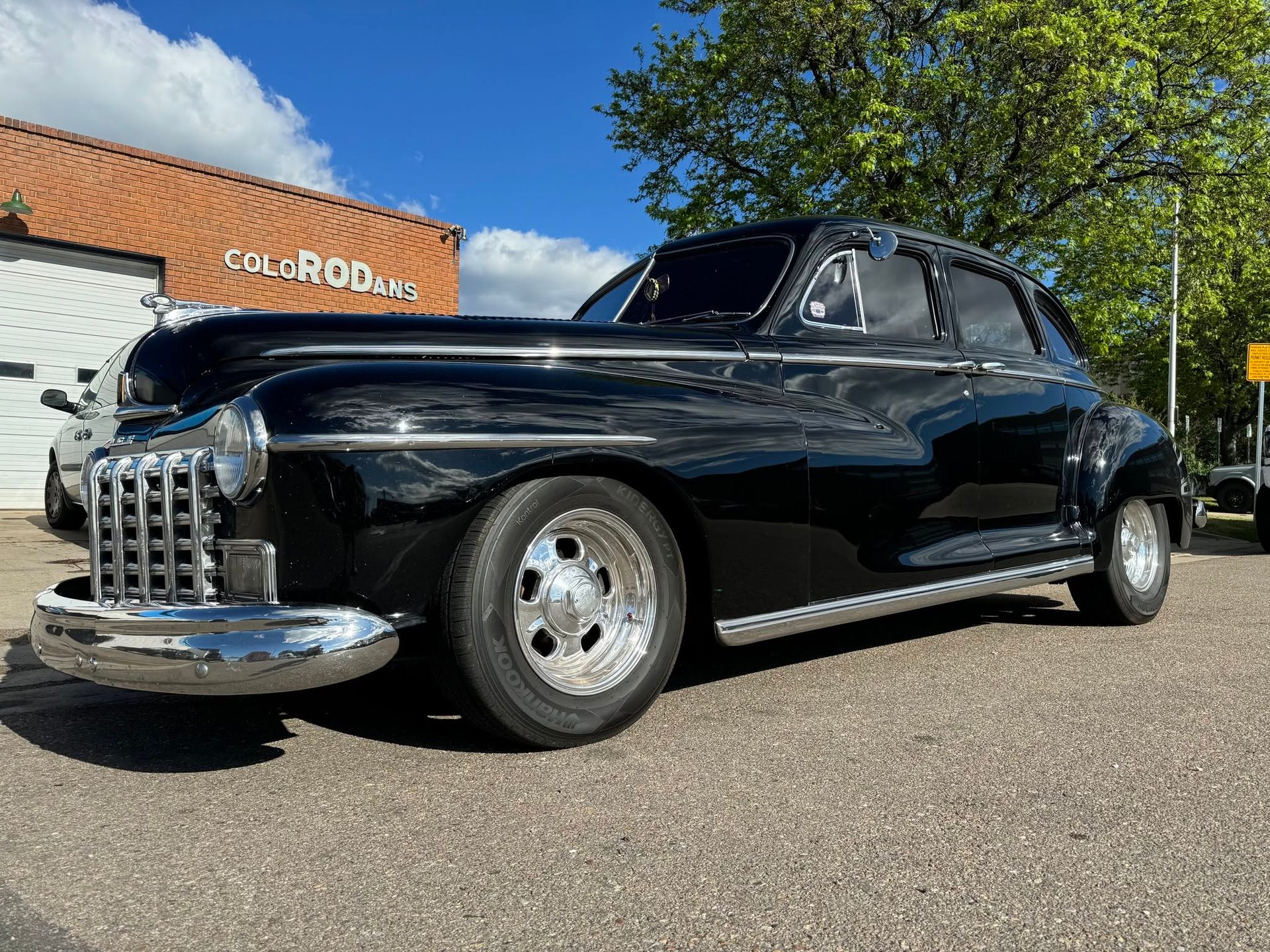 Black classic coupe parked outdoors by a brick building under a blue sky