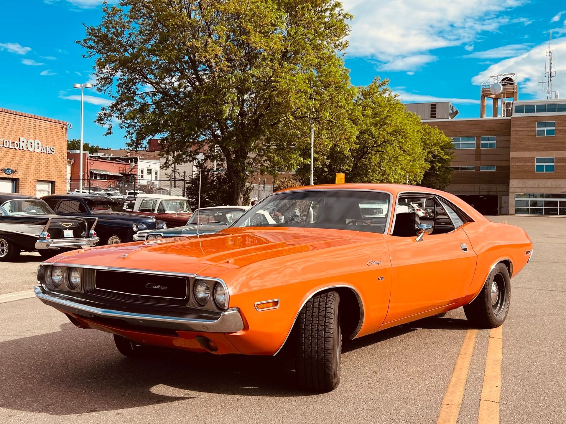 Orange classic muscle car parked on a street with brick buildings and a tree in the background