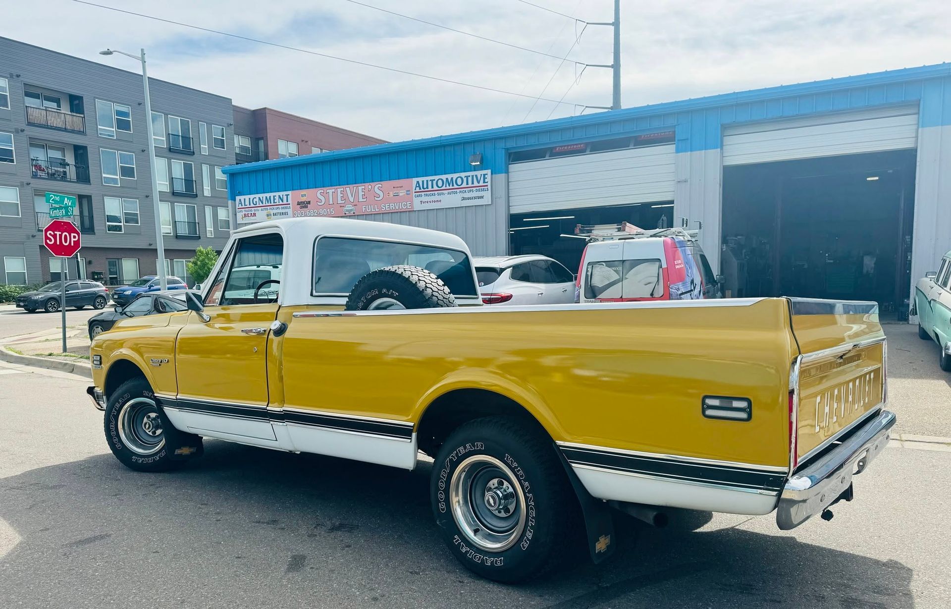Yellow classic convertible lowrider parked on a street in front of auto repair shops.