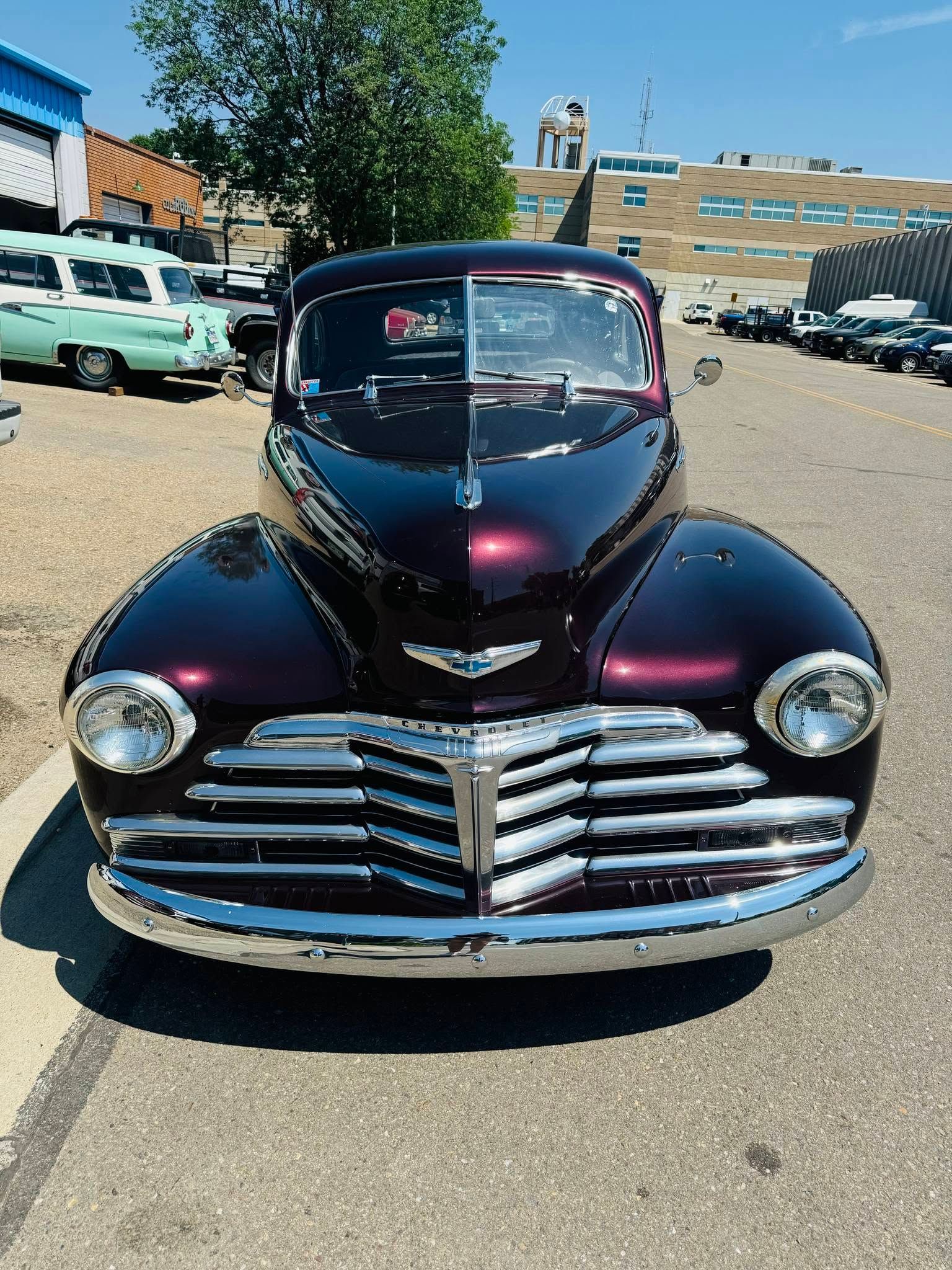 Front view of a shiny black vintage car with chrome grille parked outdoors at a car show.