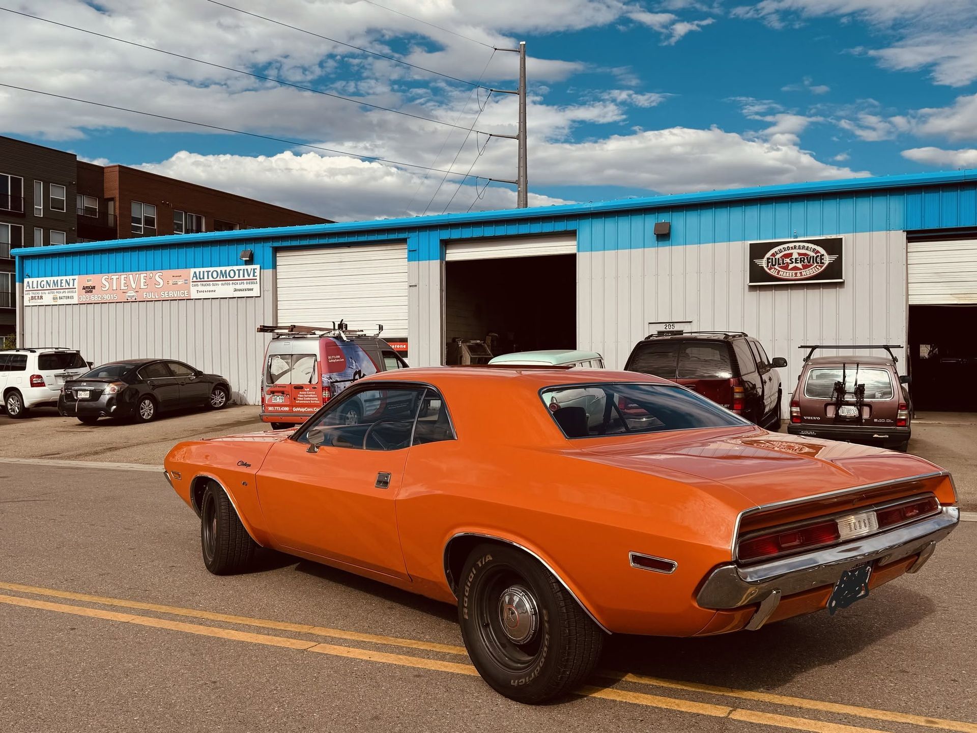Orange classic muscle car parked outside an auto shop under a cloudy sky