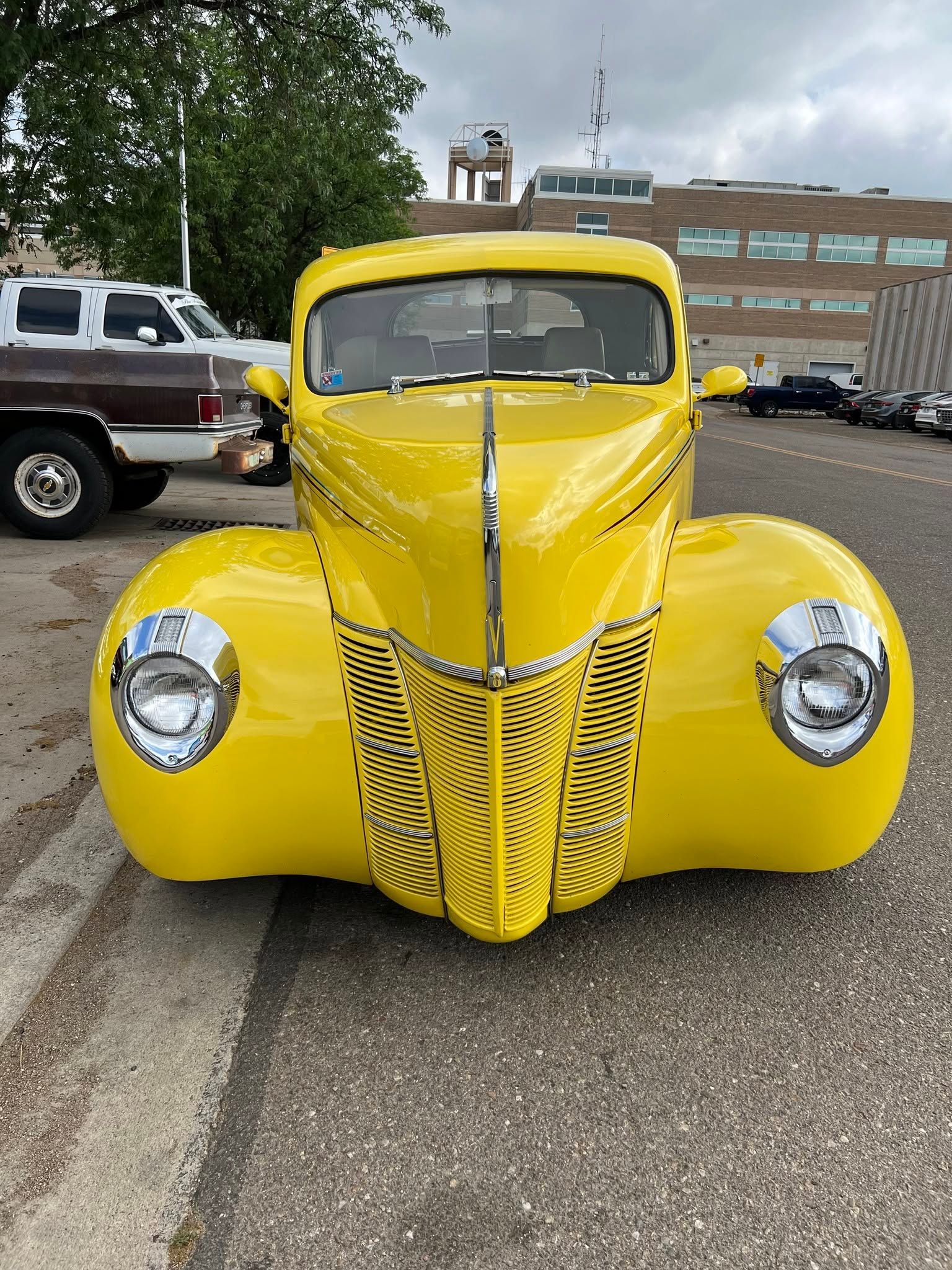 Front view of a bright yellow vintage hot rod with chrome details parked outdoors.