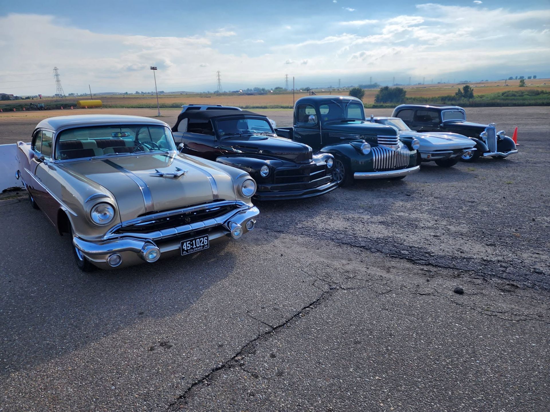 Three classic cars parked side by side on a gravel lot under a cloudy sky