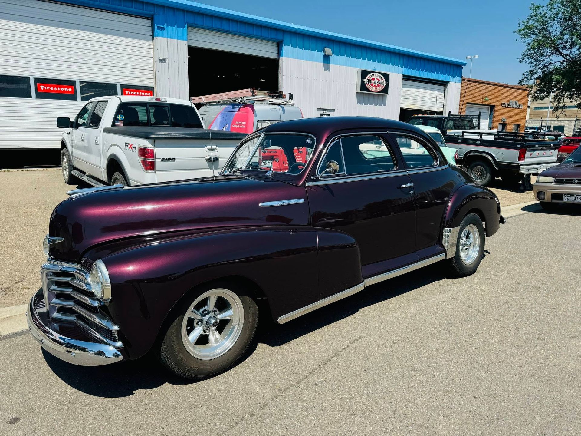 Classic dark purple vintage car parked outside a shop on a sunny day