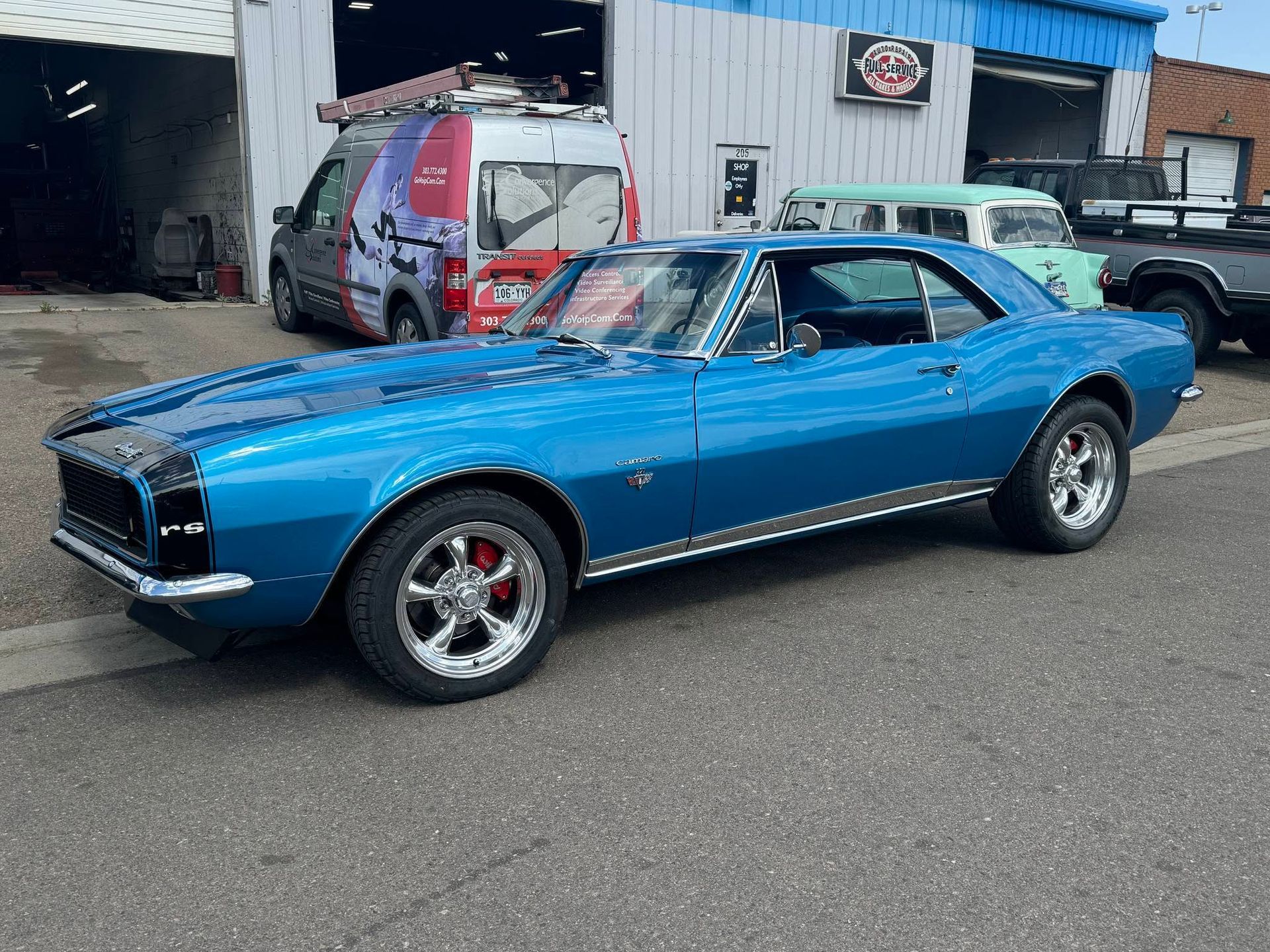 Blue classic muscle car parked outside an auto shop, side view with chrome wheels