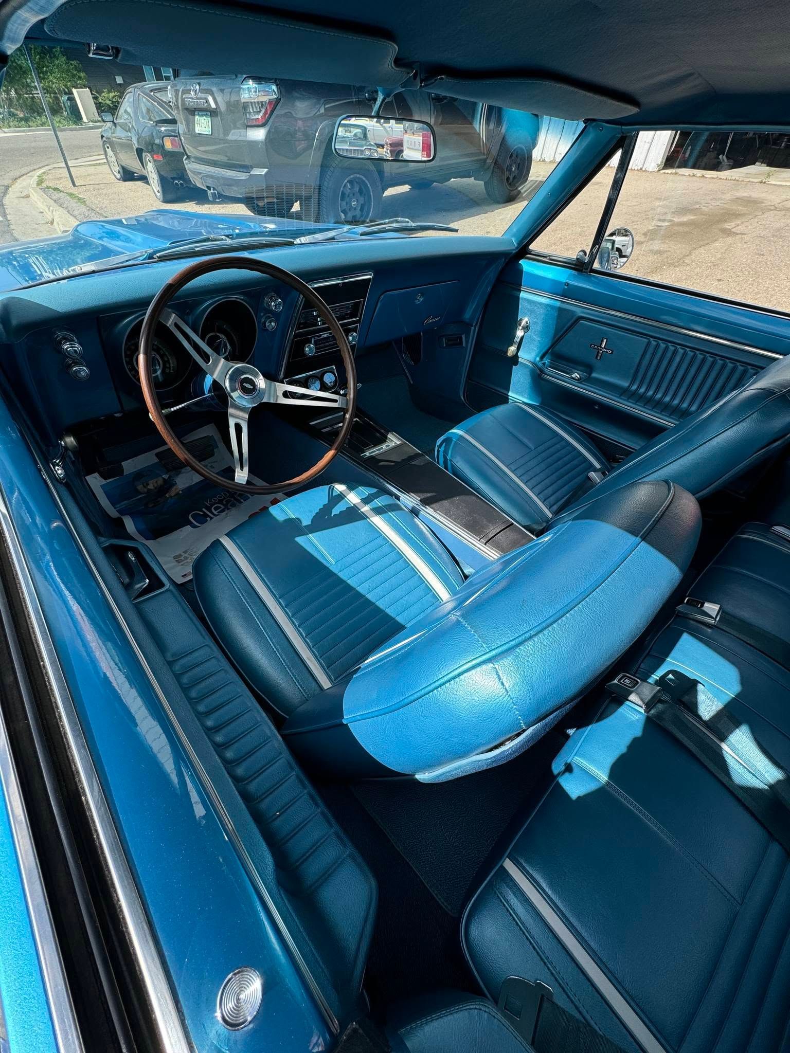 Blue classic car interior with vinyl seats, chrome steering wheel, and dashboard view through windshield