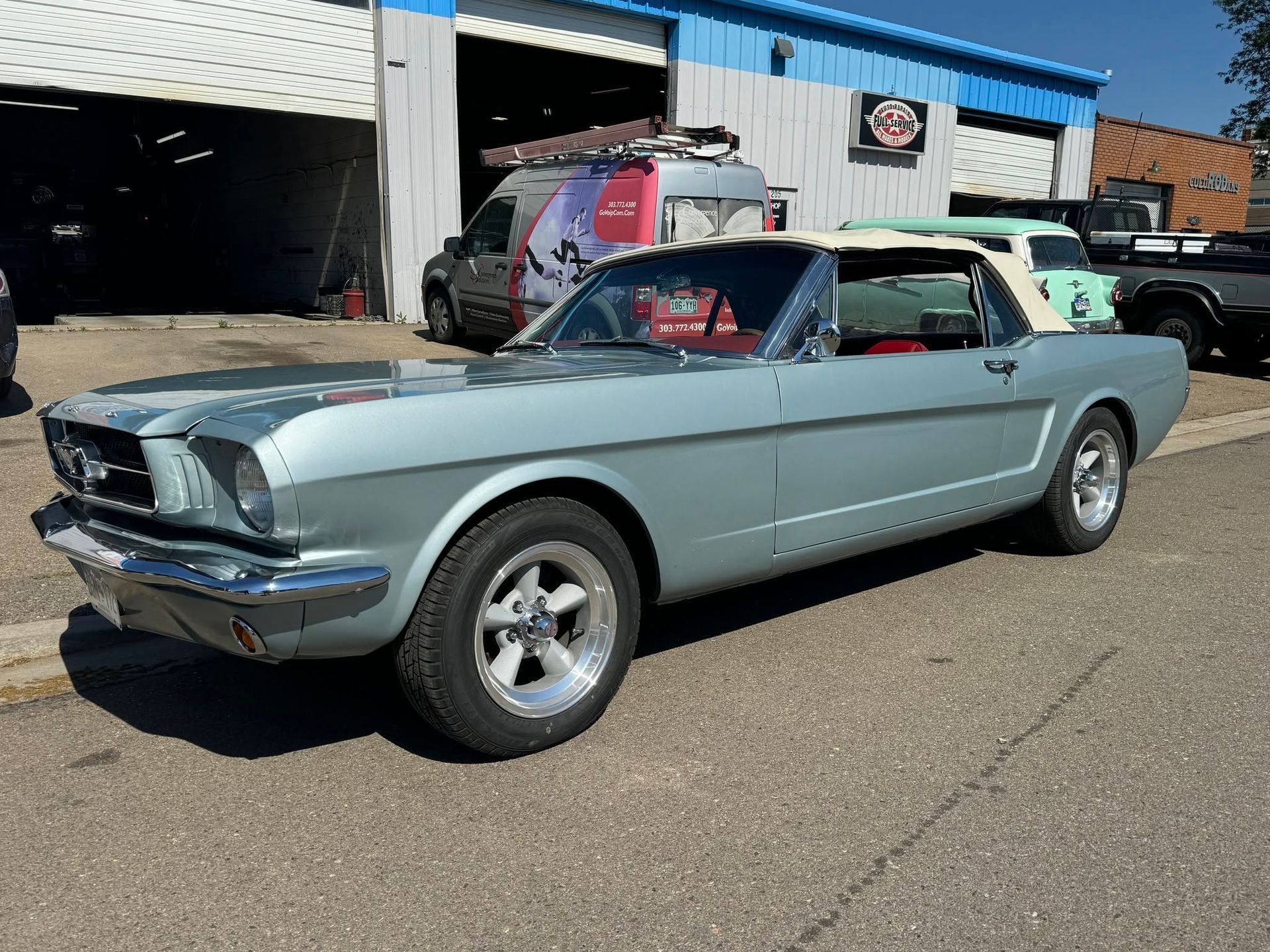 Light blue classic Ford Mustang parked outside a garage on a sunny day