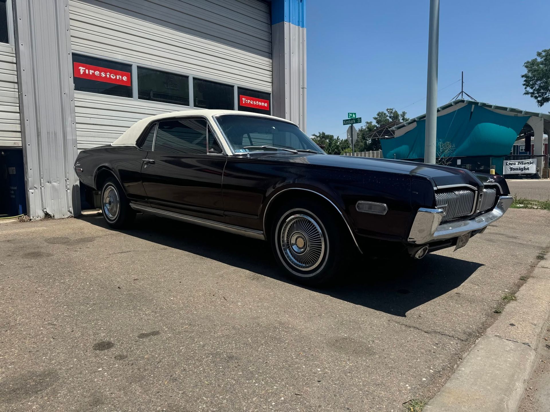Black classic convertible parked outside a garage in bright sunlight