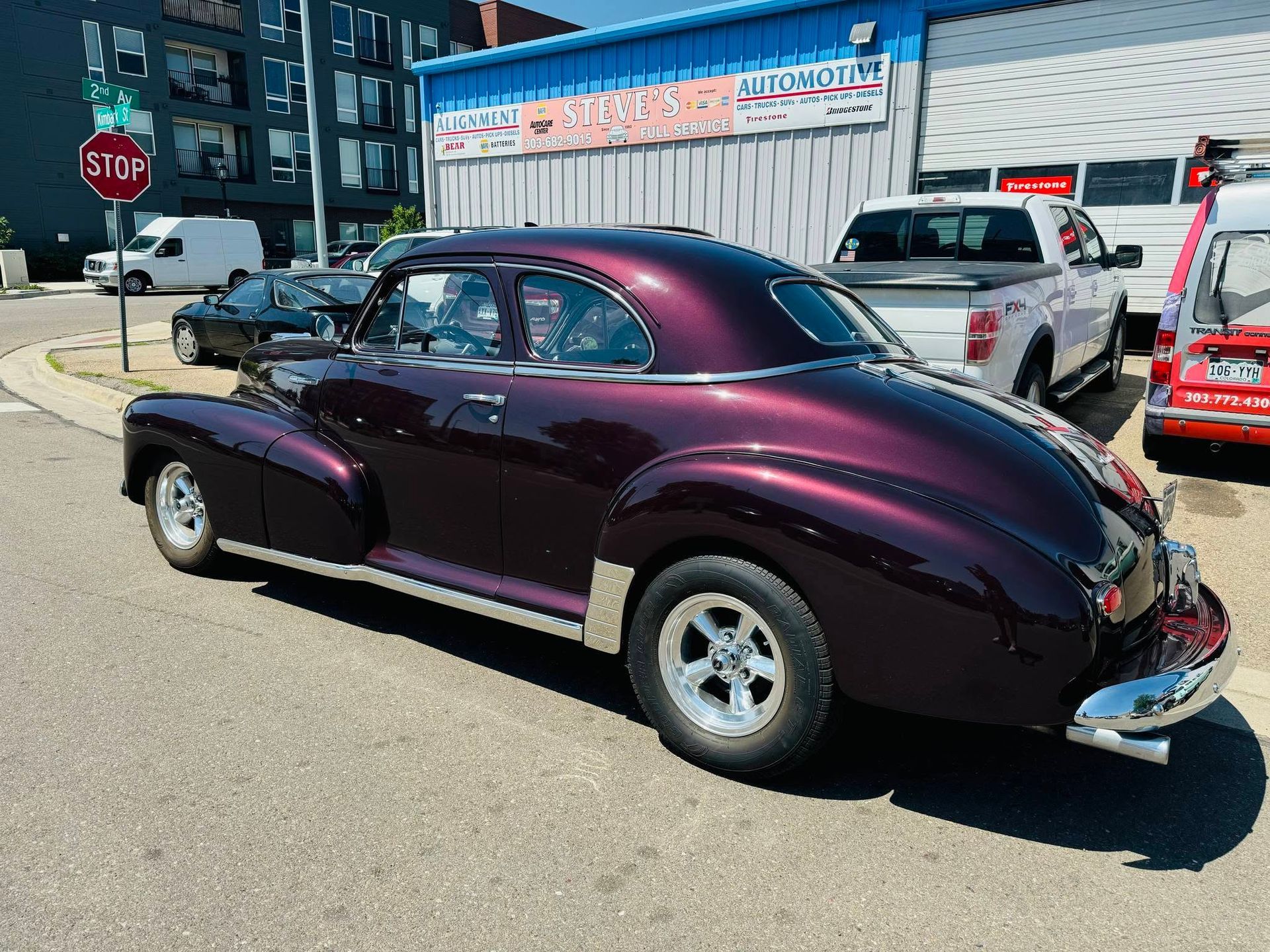 Purple classic car parked on a street near a stop sign and storefronts