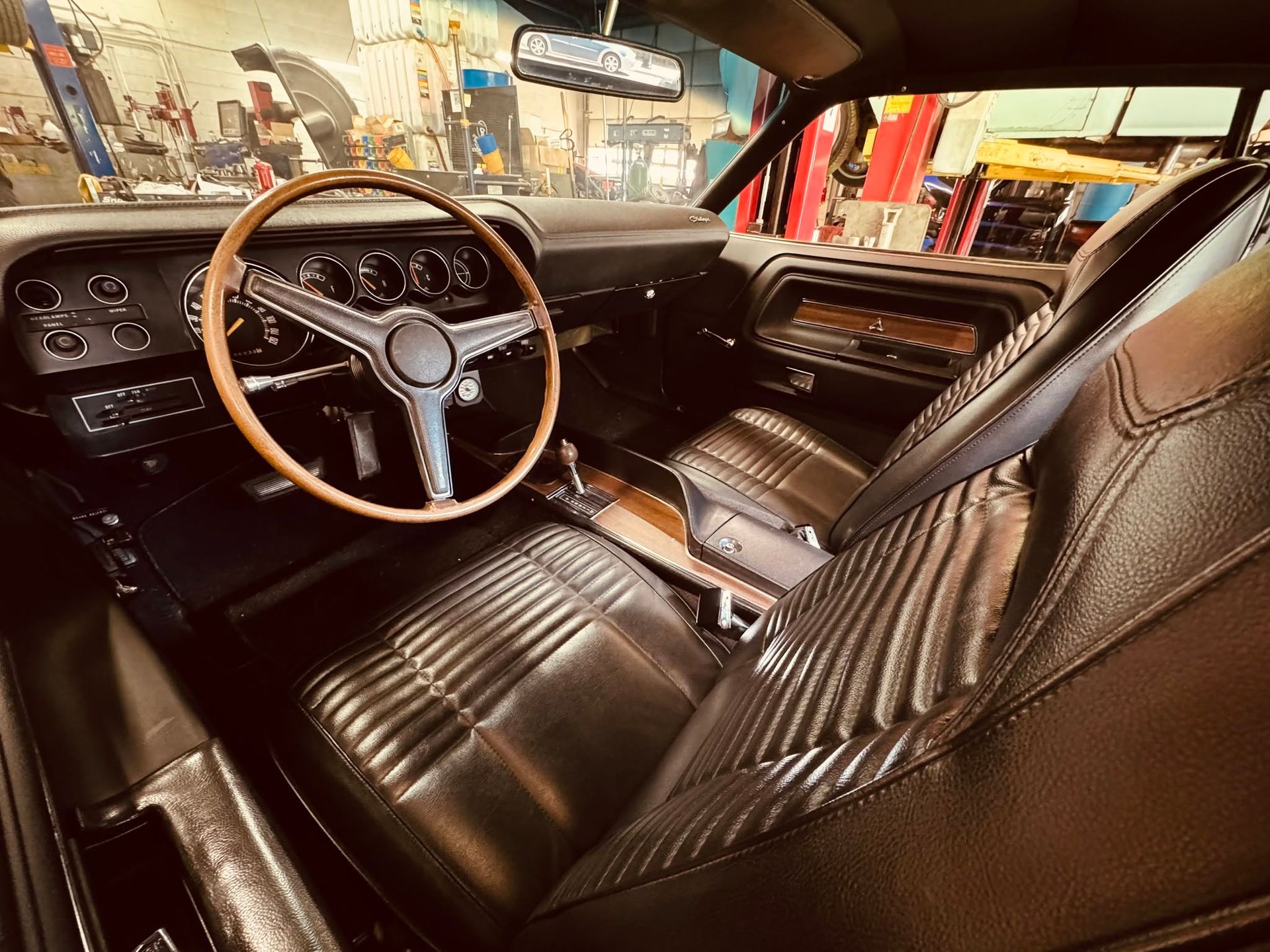 Classic car interior with black leather seats, wood steering wheel, and dashboard in a garage