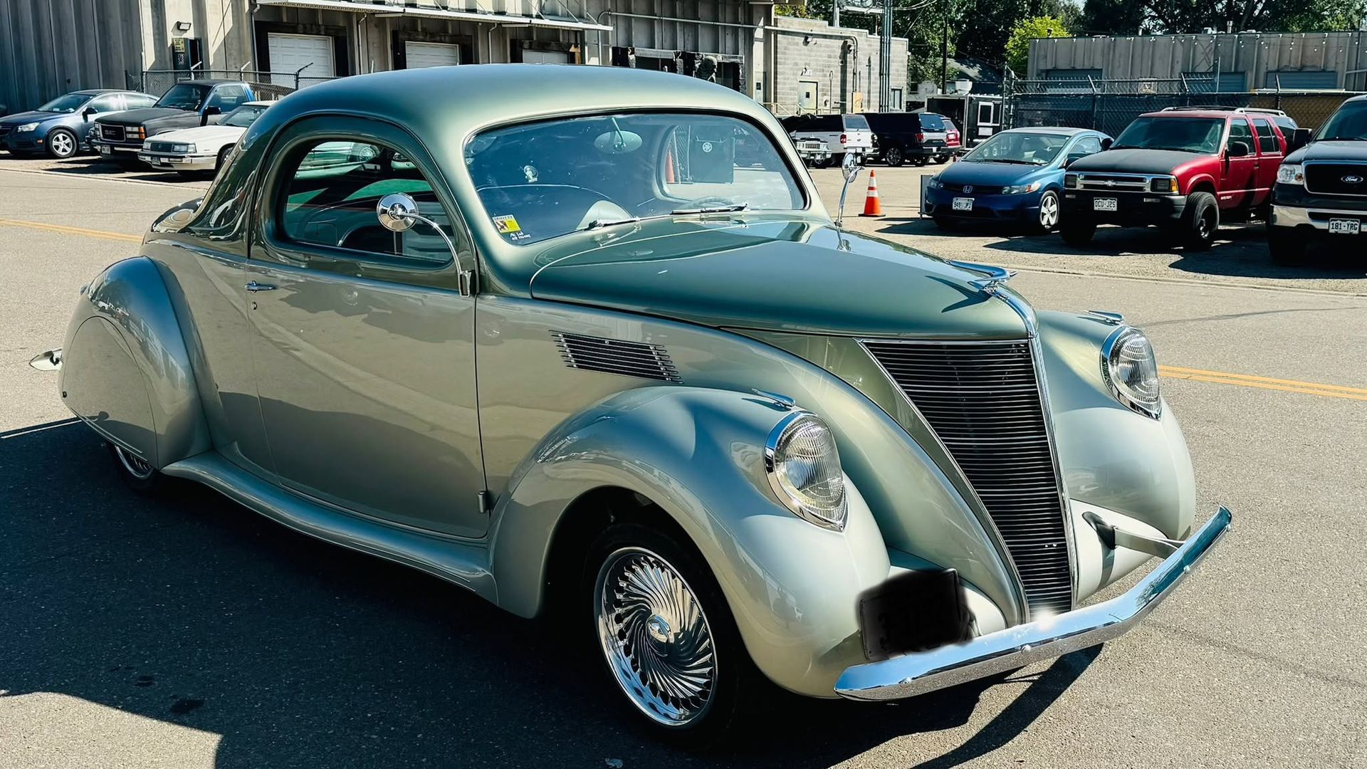 Silver vintage coupe parked on a sunny street, front view with rounded fenders and chrome grille