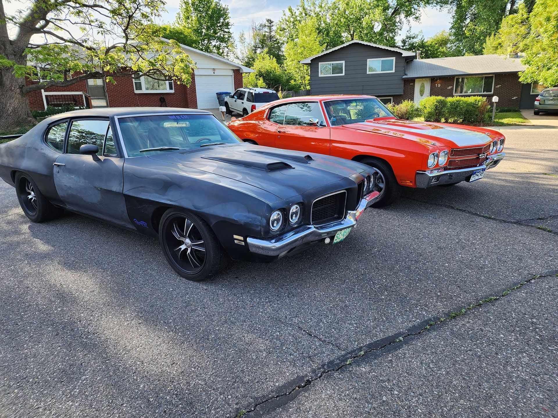Two classic muscle cars, black and red, parked side by side on a suburban street.