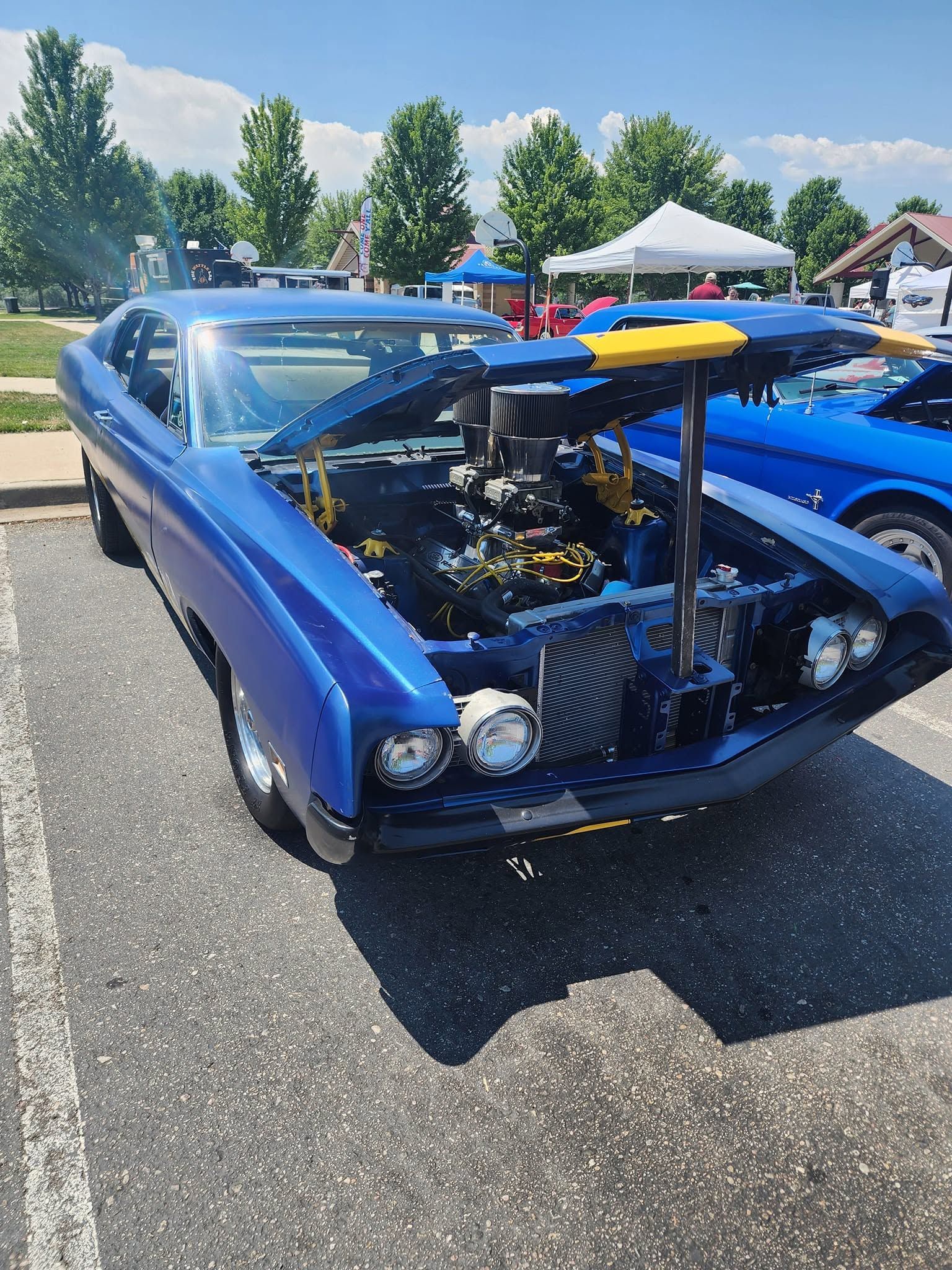 Blue custom hot rod with exposed engine parked outdoors at a car show