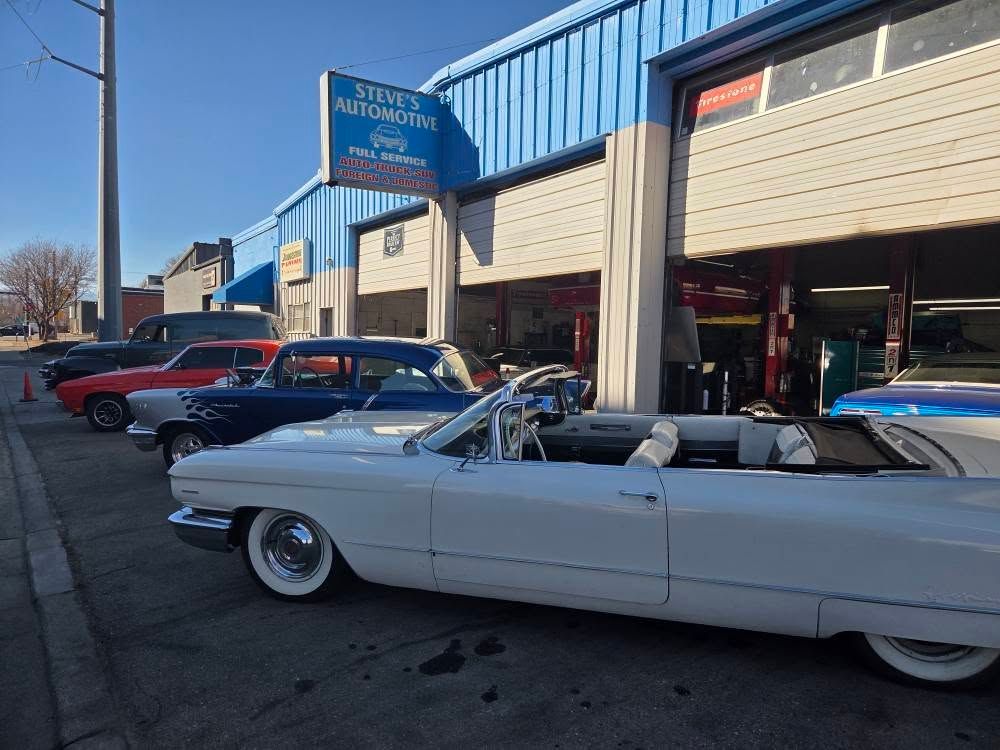 Classic cars parked outside an auto shop, including a white convertible in front.