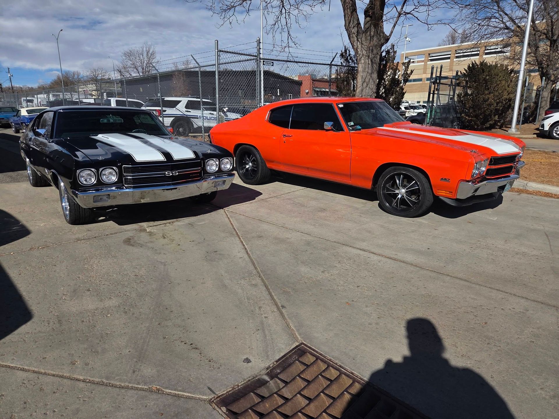 Two classic cars parked outdoors, one black with white racing stripes and one bright orange.