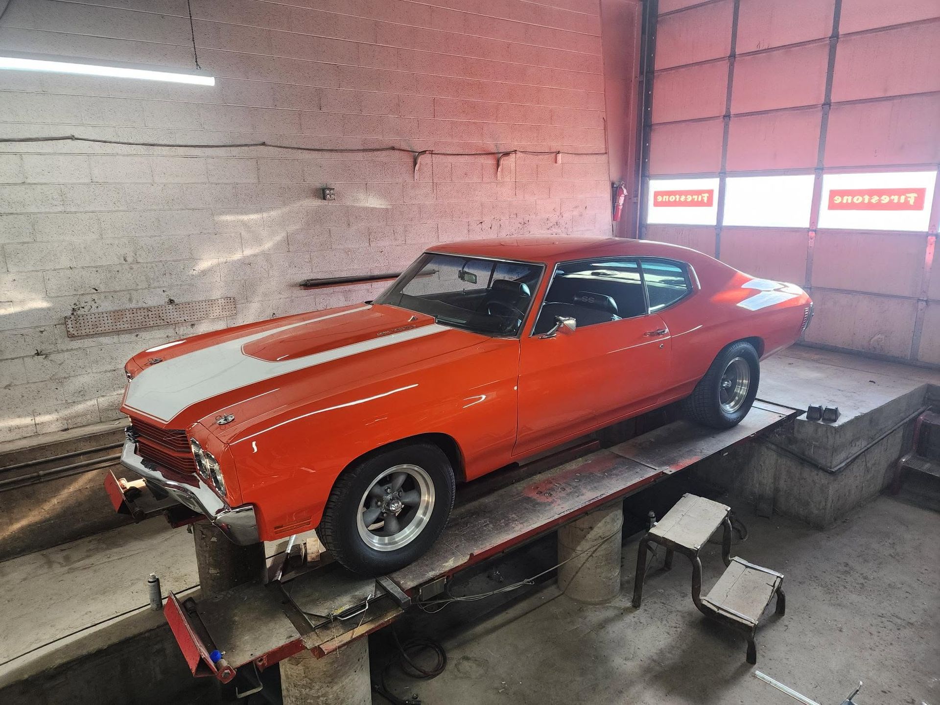 Orange classic muscle car on a dynamometer in an indoor garage, with white racing stripes