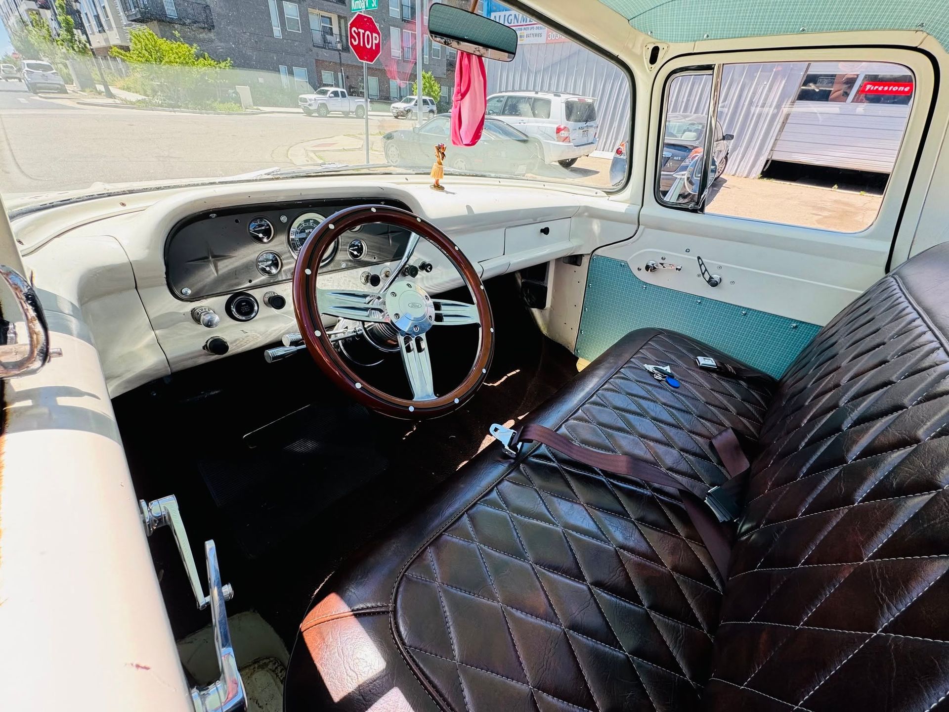 Vintage car interior with cream walls, wood steering wheel, and black tufted bench seat.