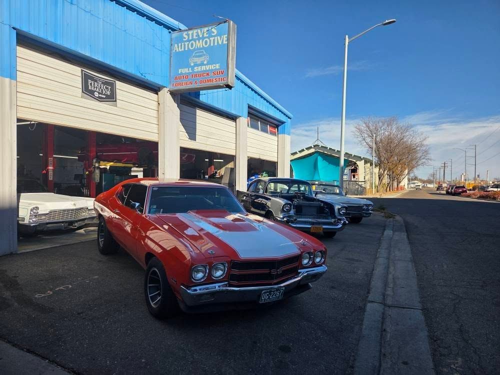 Classic orange muscle car parked outside an auto shop on a sunny street.