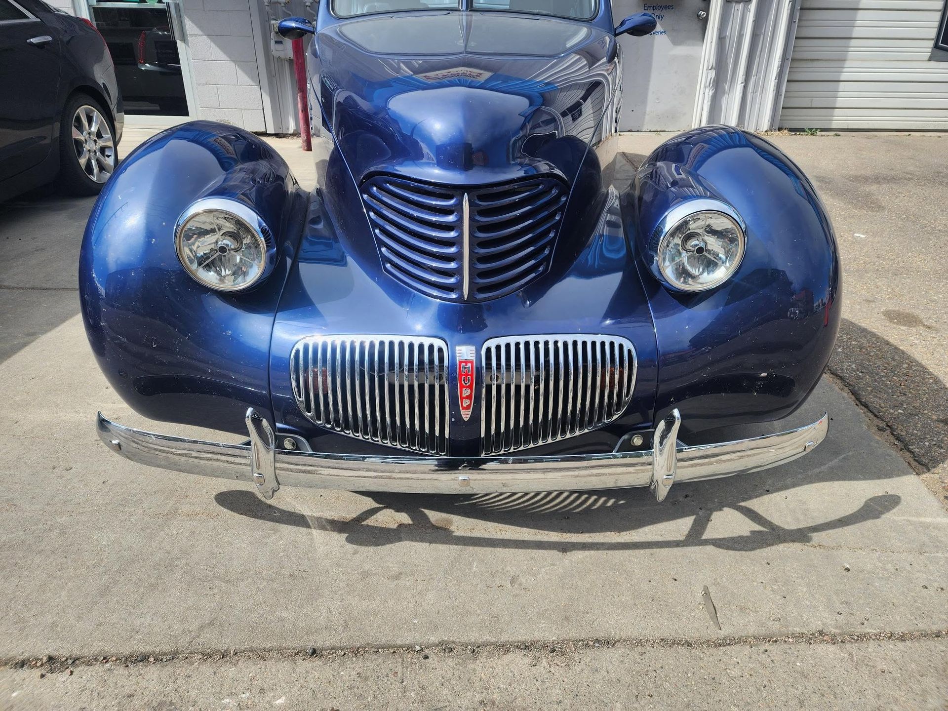 Blue vintage car front view parked on pavement with chrome grille and round headlights