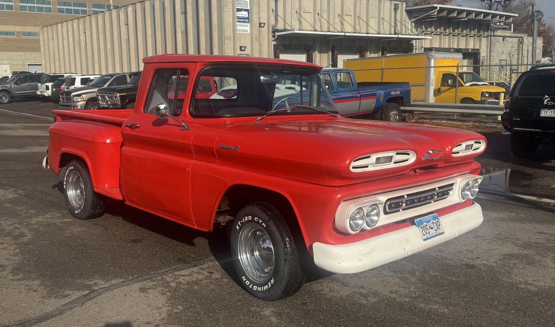 Red classic pickup truck parked outdoors in front of buildings, side view.