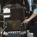 Person points to a black radiator and battery setup in a garage or workshop