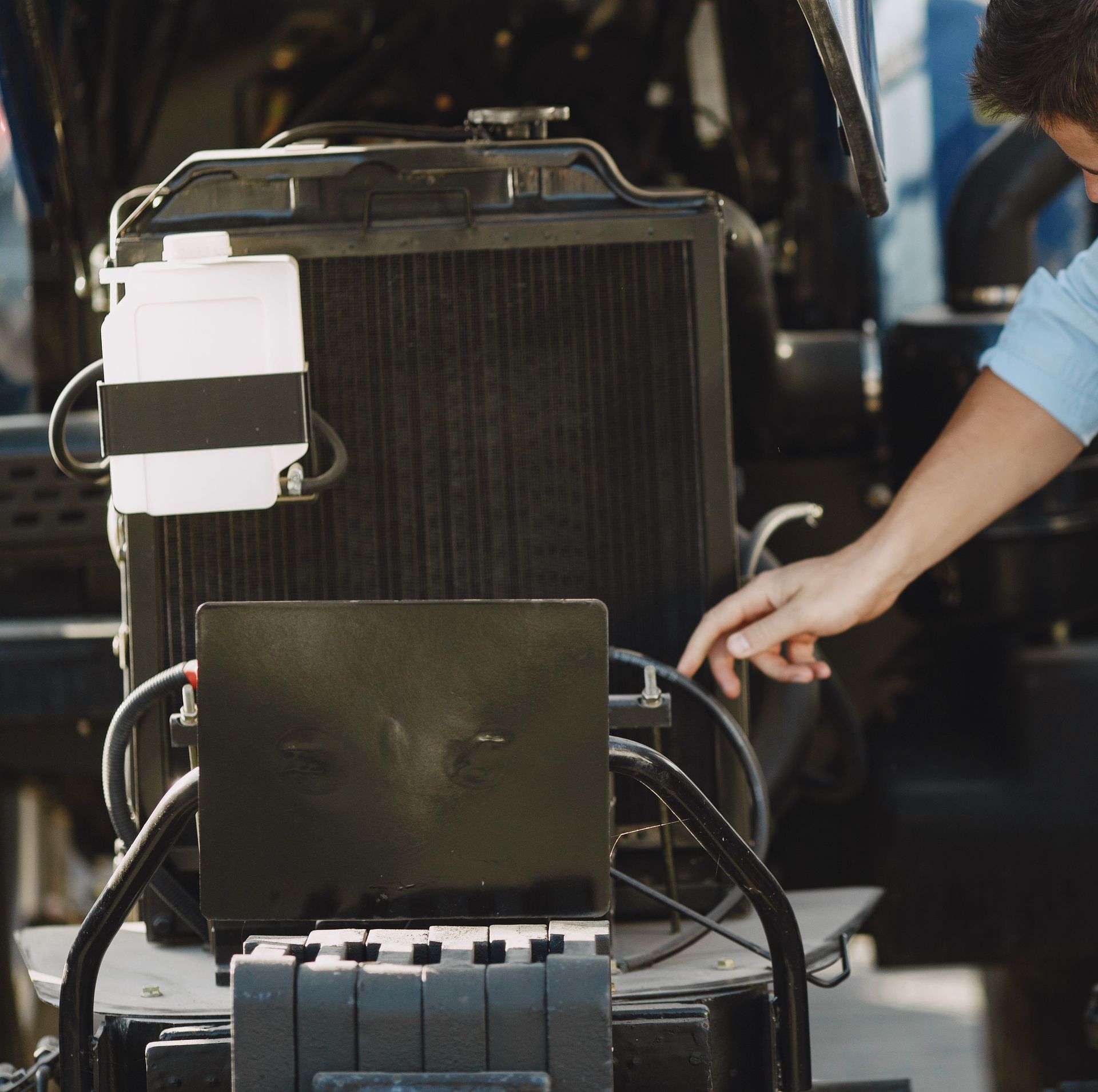 Person points to a black radiator and battery setup in a garage or workshop