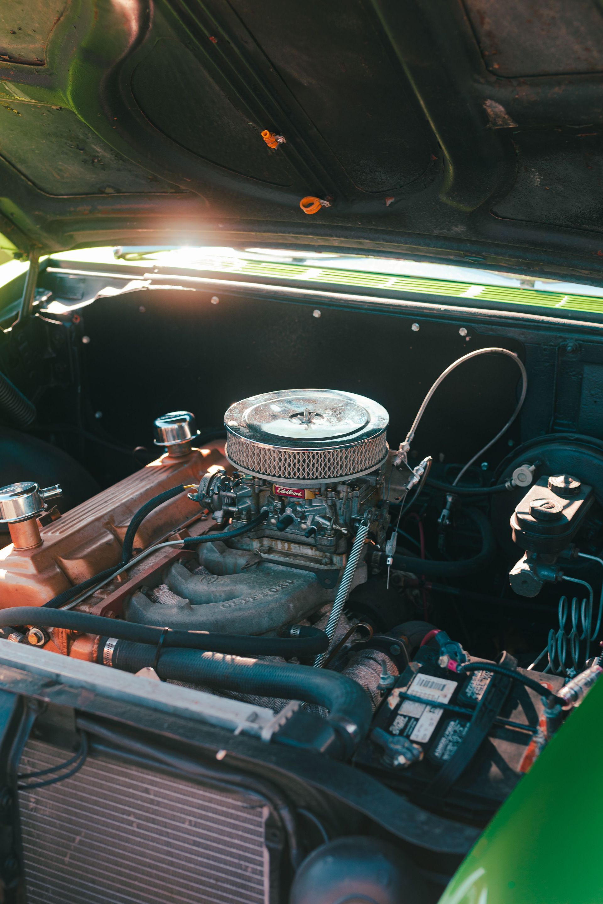 Classic car engine bay with chrome air filter, hoses, and radiator under an open hood