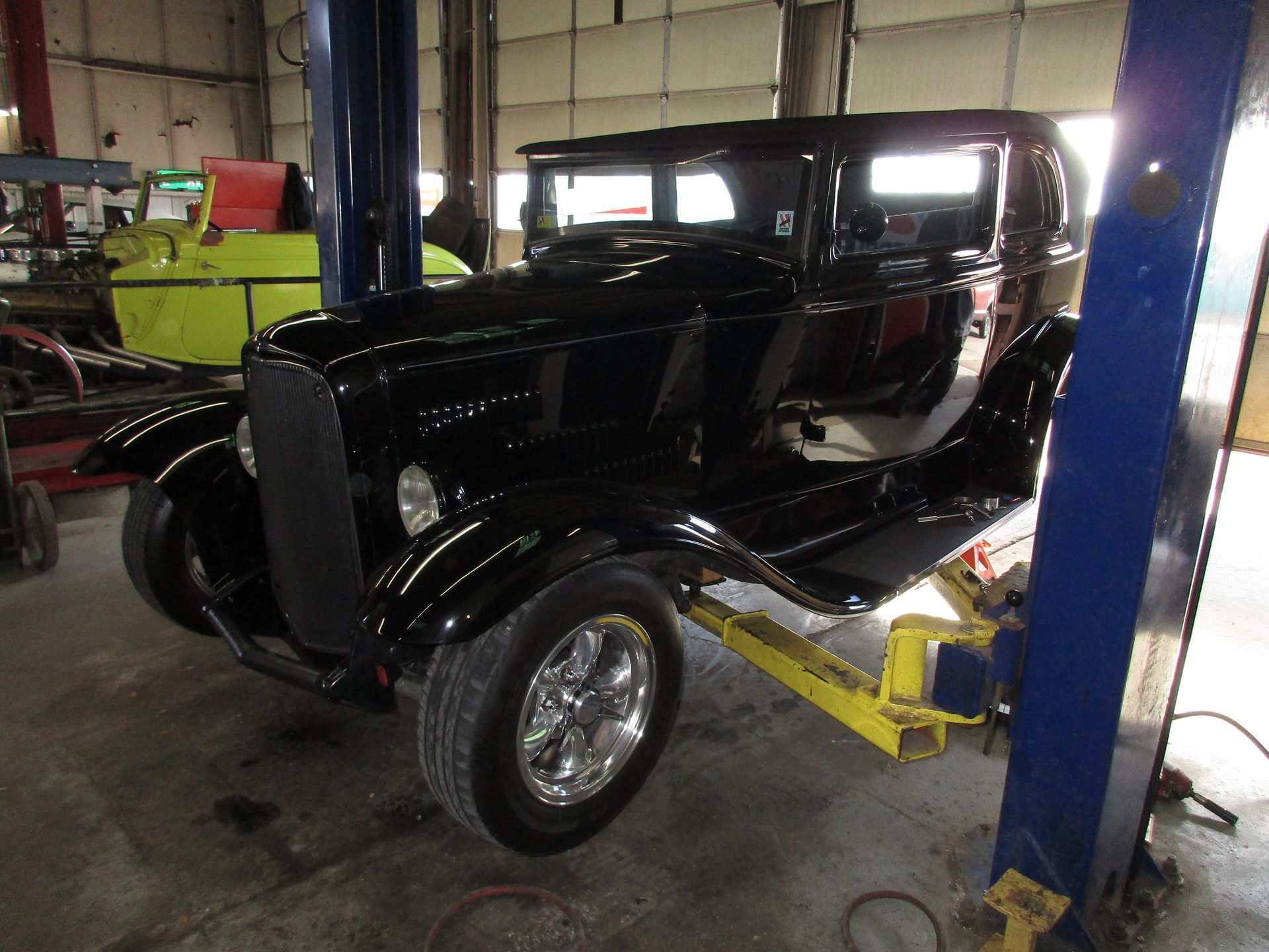 Black vintage hot rod on a lift inside an auto shop, with shiny chrome wheels and a black body.