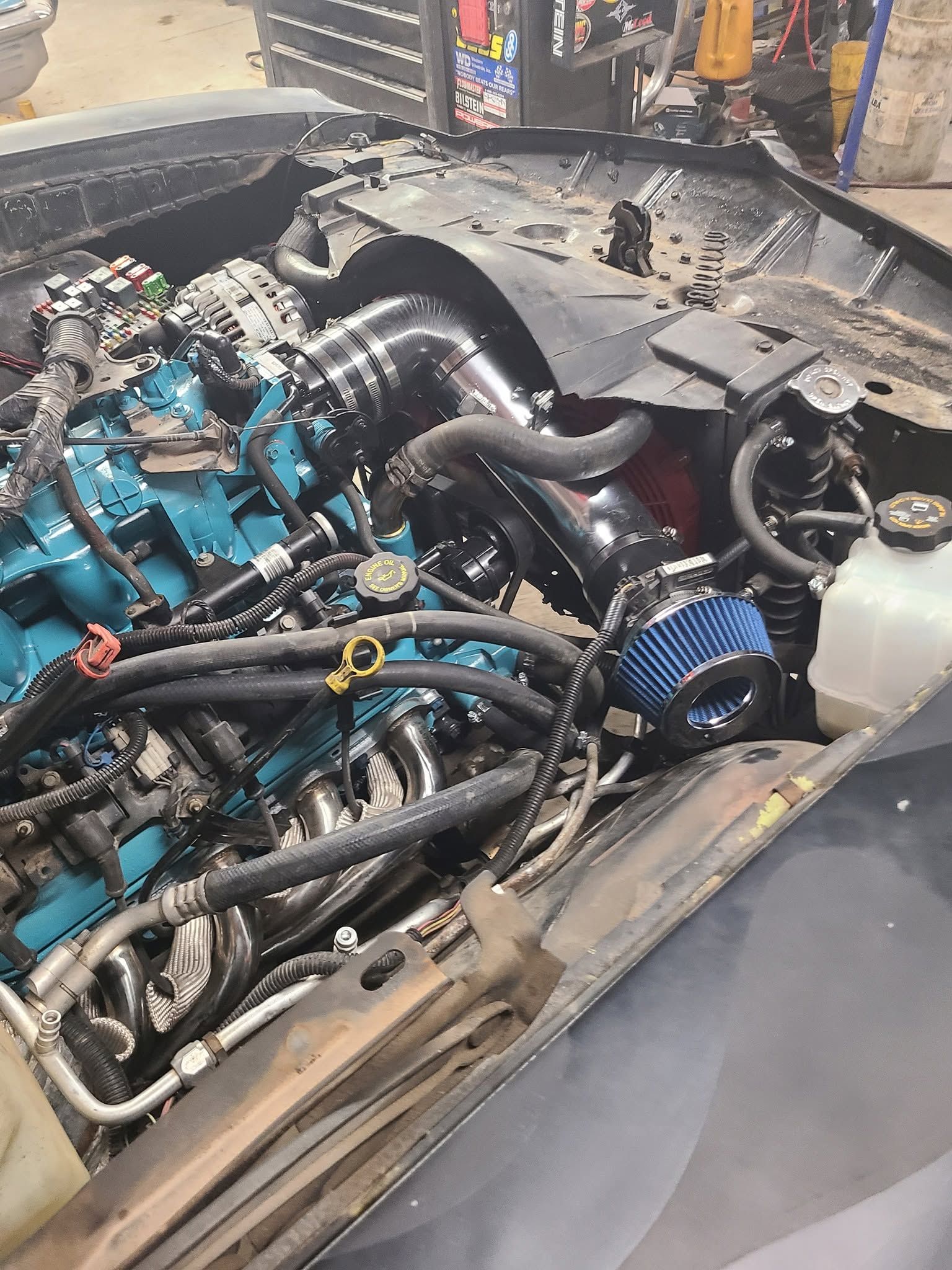 Car engine on a stand, with blue intake piping and exposed hoses in a workshop.