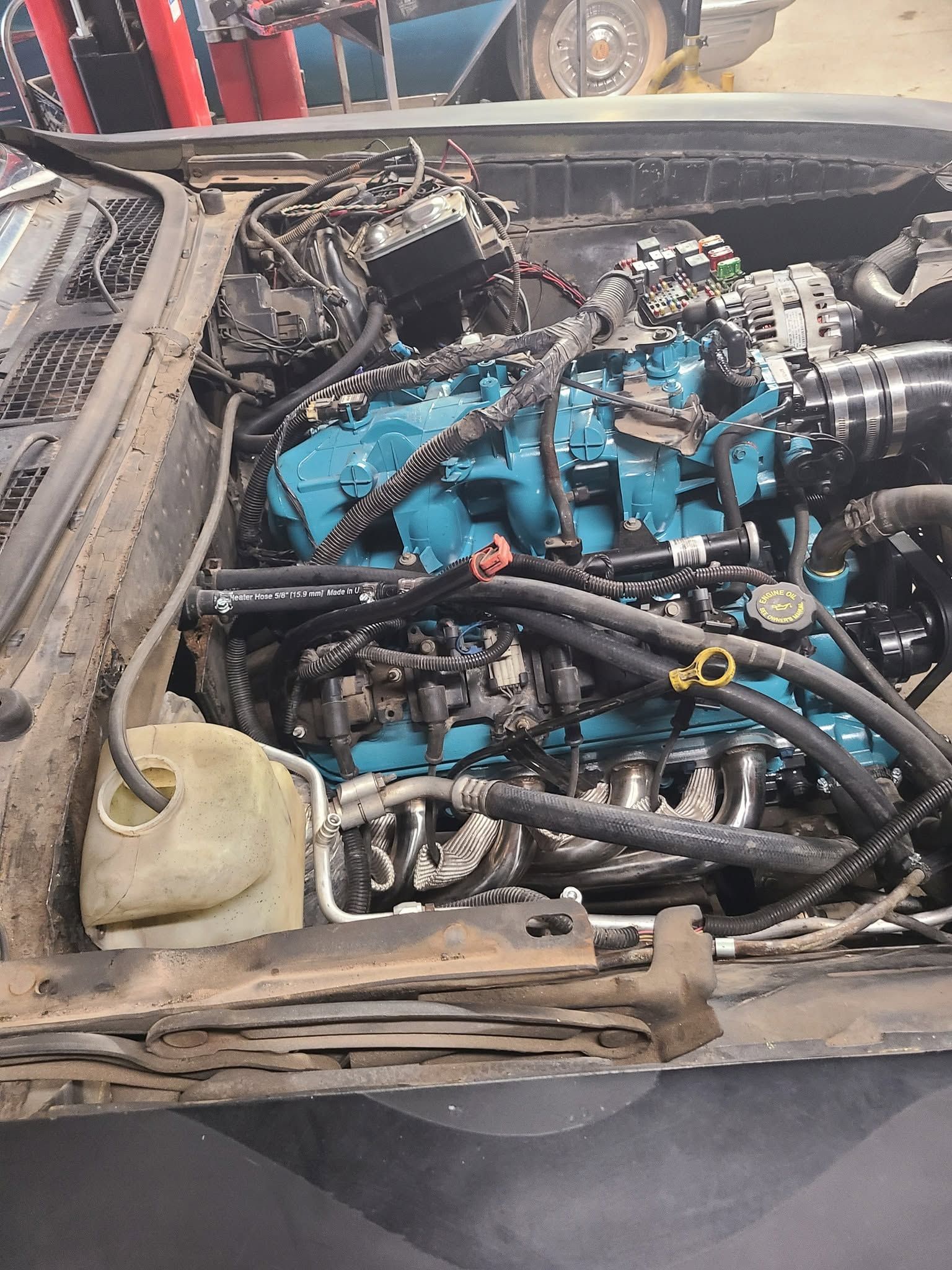 Blue engine in a dusty car bay with hoses and wiring exposed under the hood