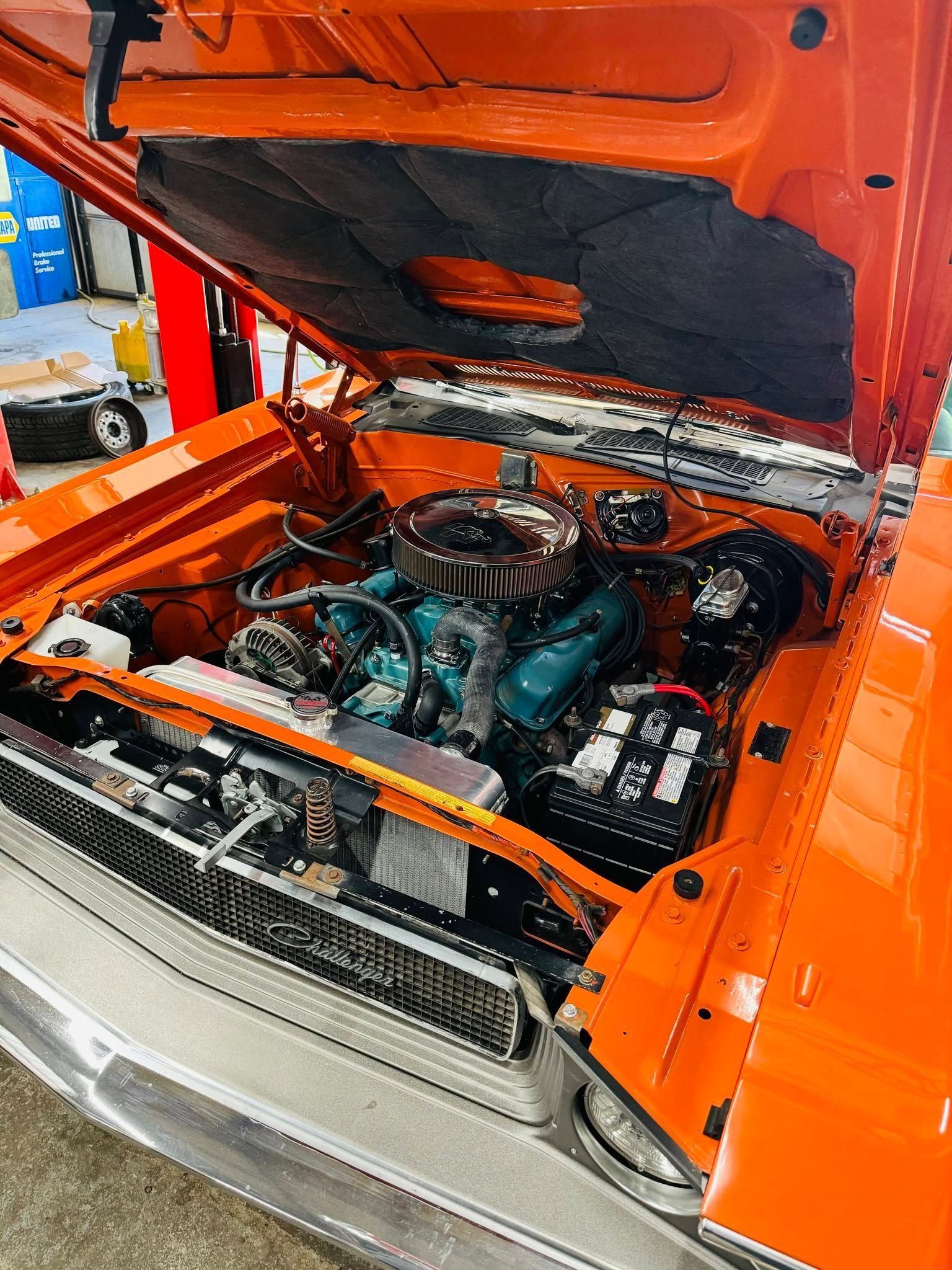 Classic orange car with hood open, showing a detailed turquoise engine in a garage.