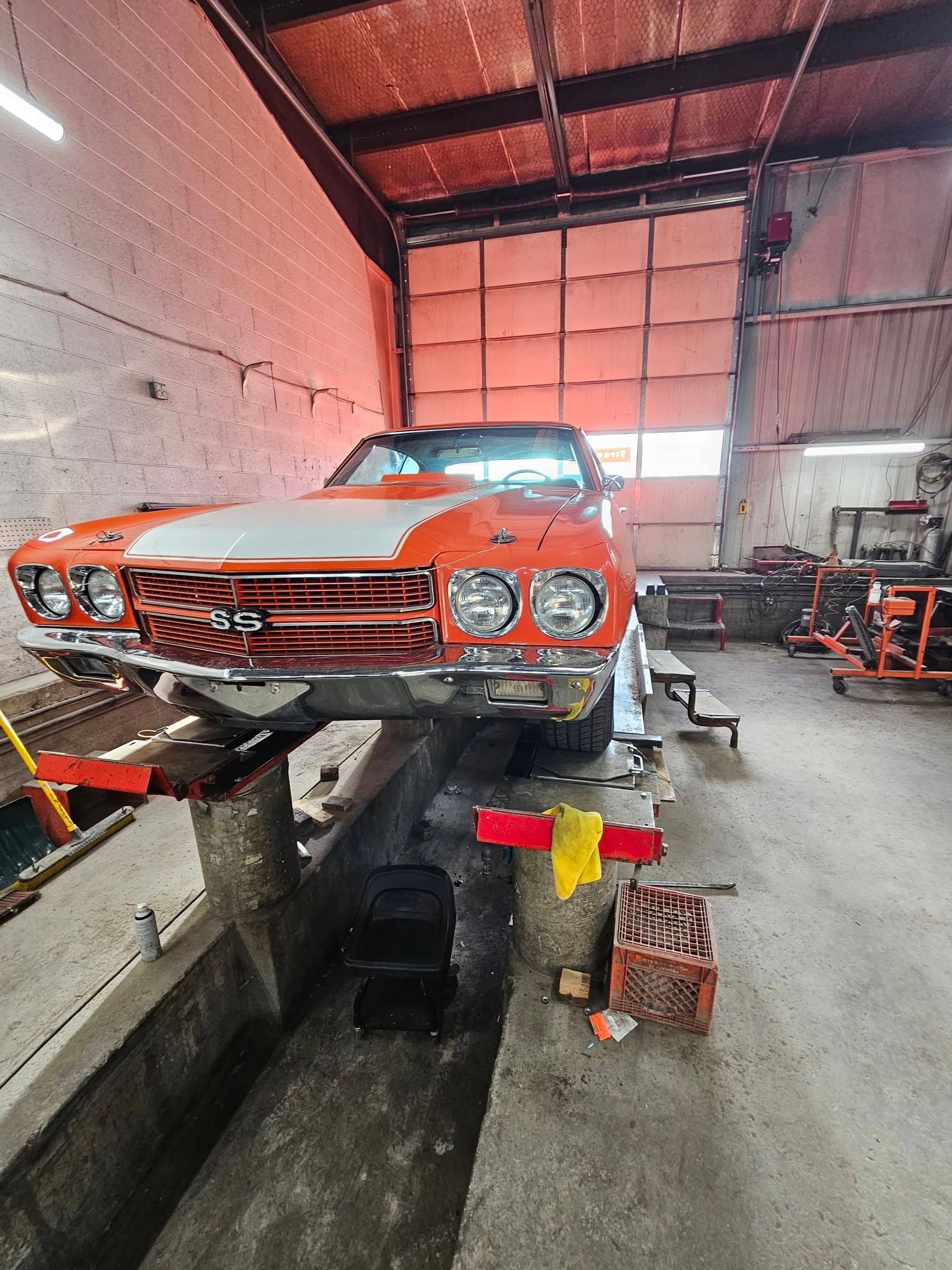 Orange classic car on a lift inside an auto shop garage, with tools and equipment nearby