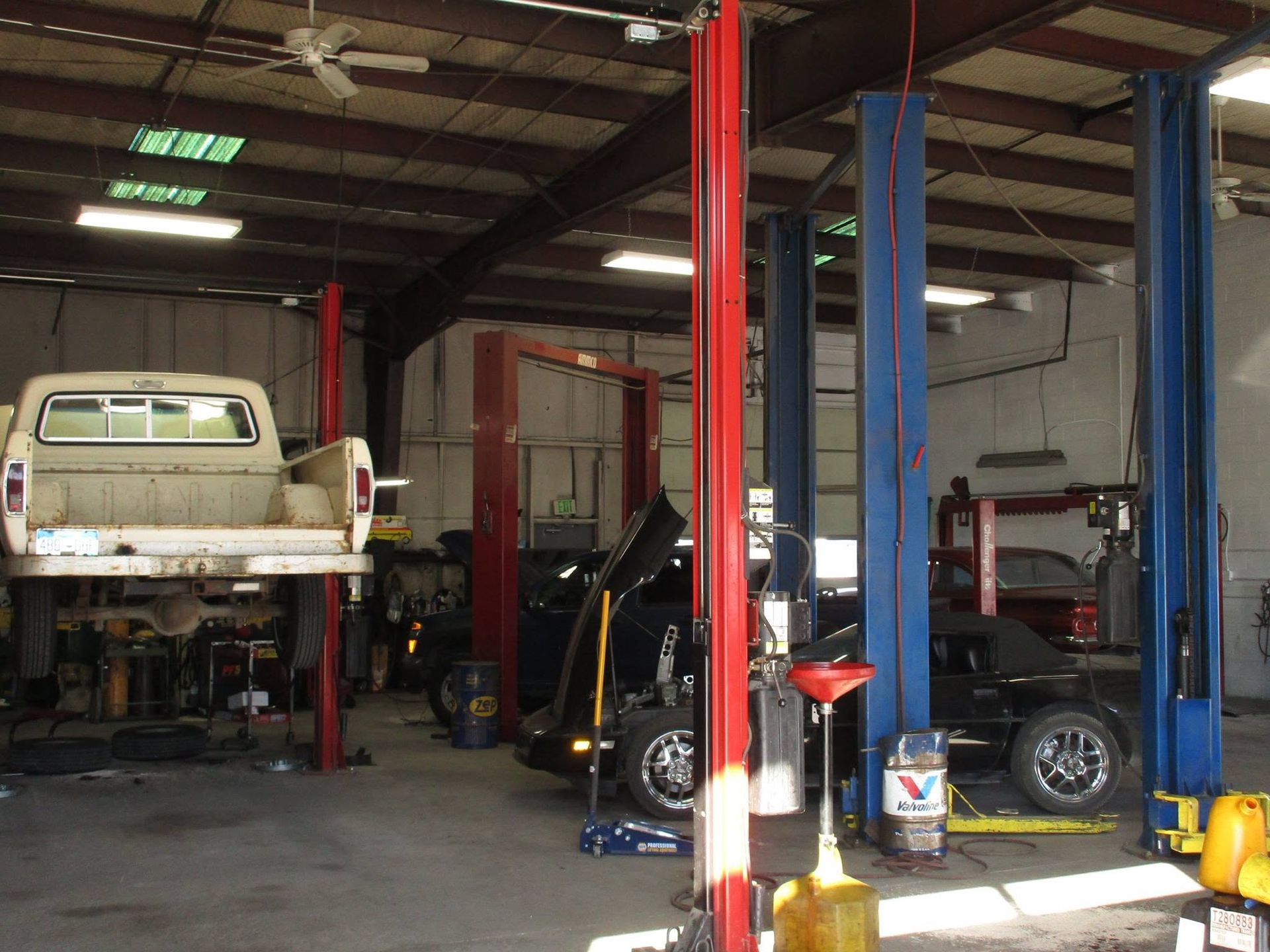 Auto repair shop with several cars on lifts and a white pickup in the foreground