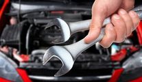Hand holding two wrenches in front of an open car engine