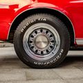 Close-up of a red car’s chrome wheel and black tire on a concrete floor.