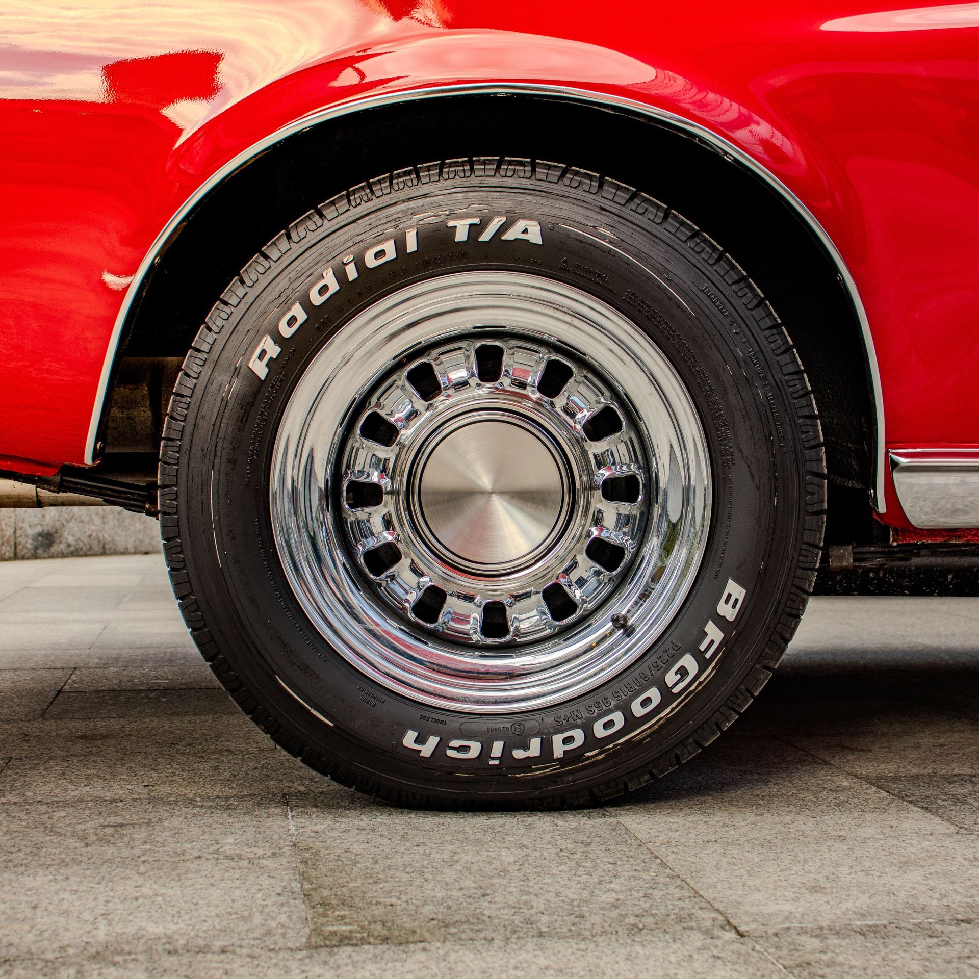 Close-up of a red car’s chrome wheel and black tire on a concrete floor.