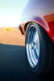Close-up of a red car’s wheel speeding along a sunny desert road