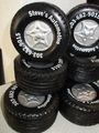 Stack of black tires with silver rims labeled “Steve’s Automotive” and phone number numbers.