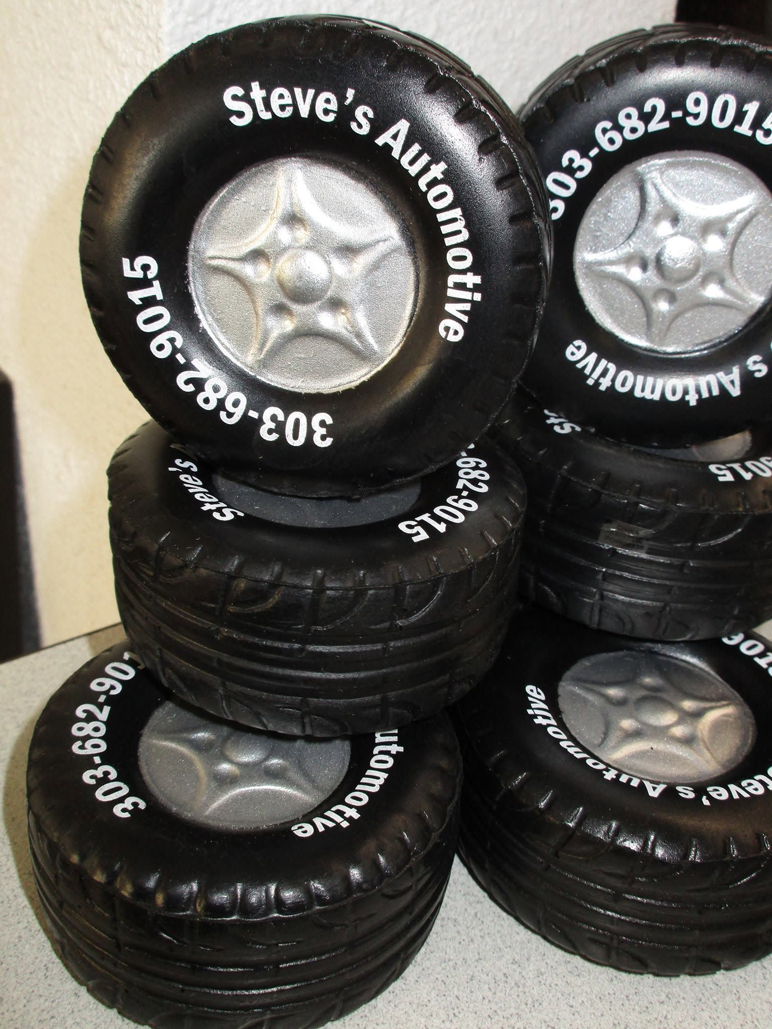 Stack of black tires with silver rims labeled “Steve’s Automotive” and phone number numbers.