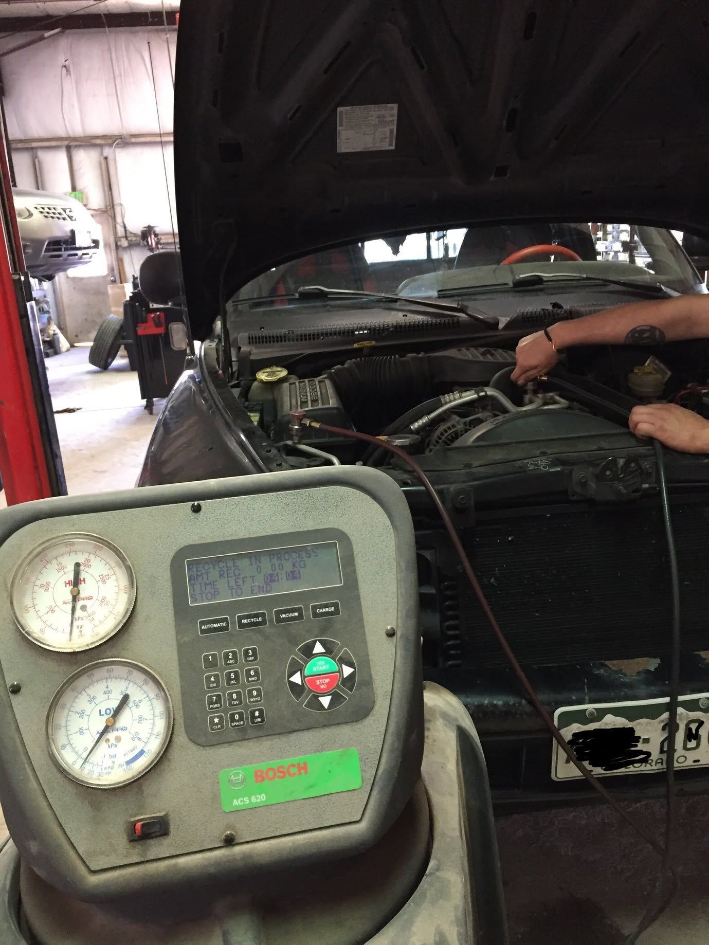 Car engine being tested in a garage with diagnostic gauges in the foreground and hood open.