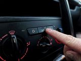 Finger pressing car climate control button on dashboard with red-lit dials