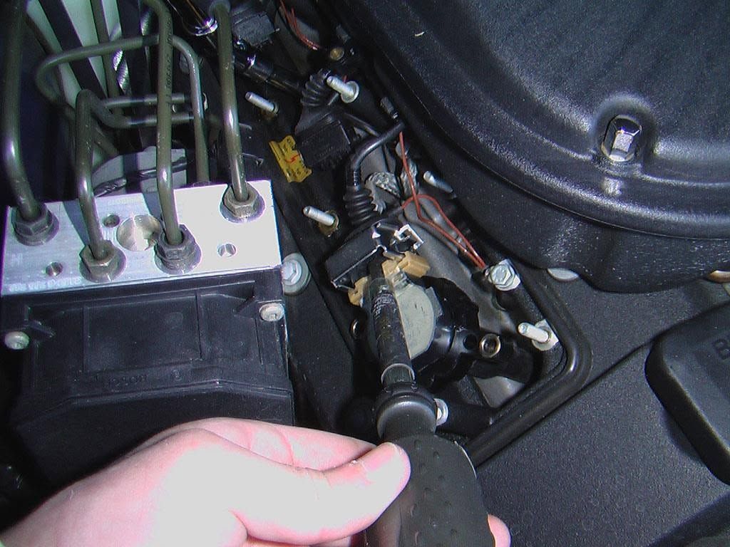 Hand near car engine bay, holding a hose next to metal components and wiring.