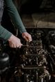 Hands adjusting engine parts in a dim garage, with rows of machinery in the background