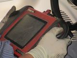 Gloved hands holding a red handheld device with a screen and cable attached
