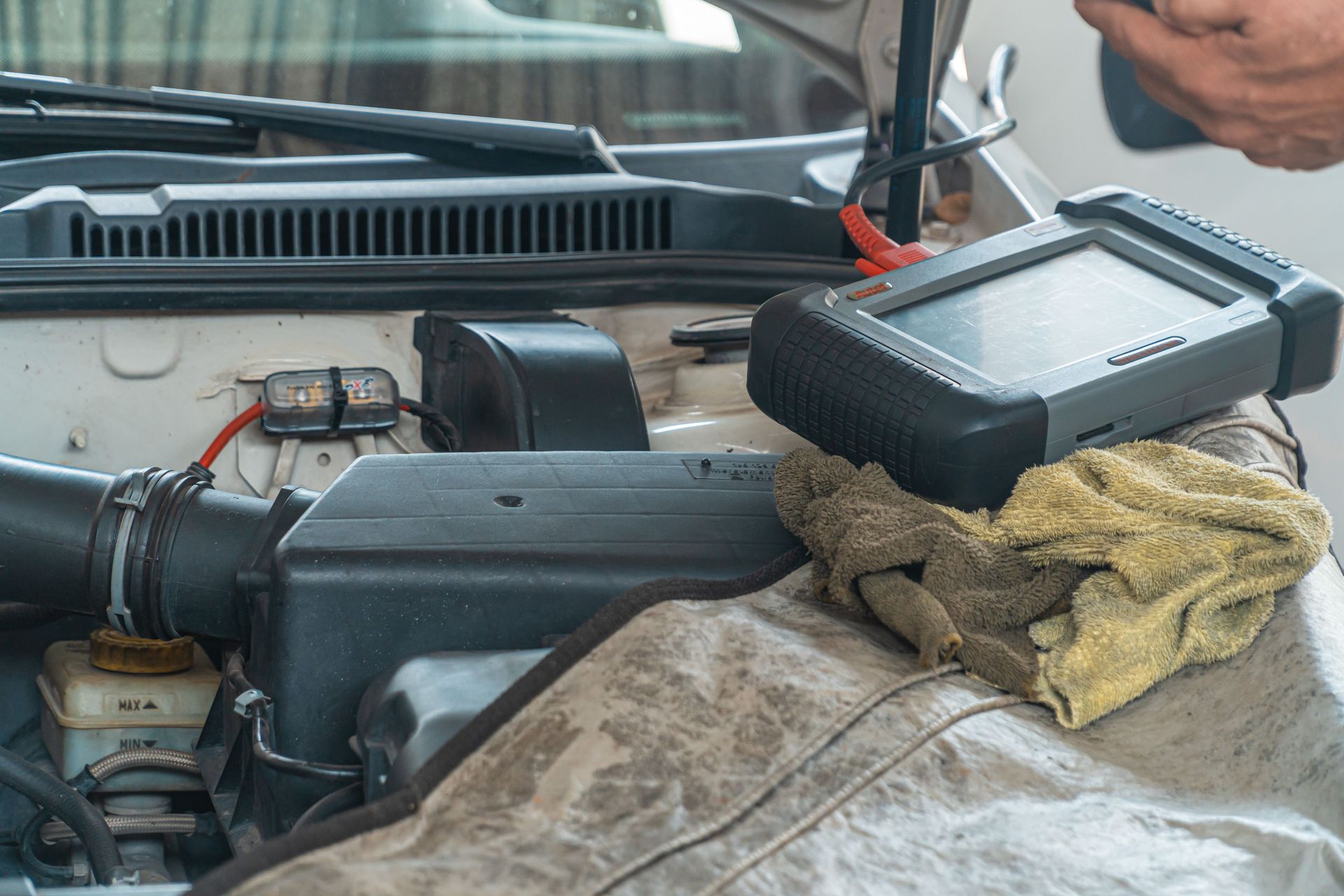 Under-hood car engine bay with a black air intake box and a dusty cloth near the windshield