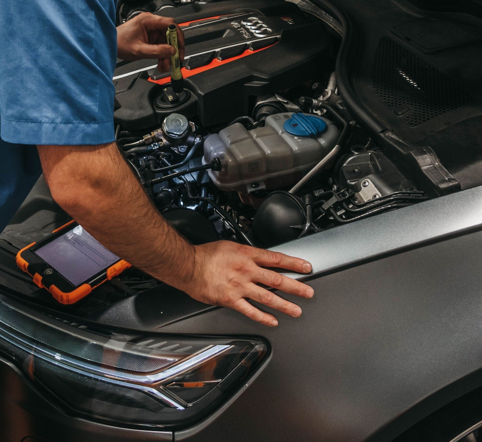 Mechanic inspecting a car engine under the hood, with a diagnostic device on the fender